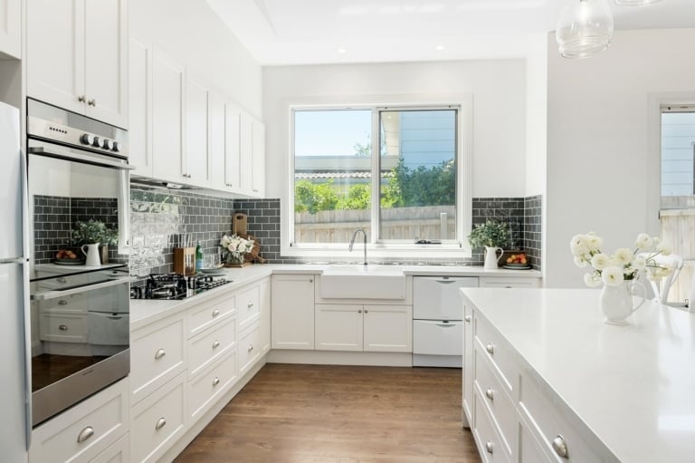 hamptons kitchen with butlers sink and white shaker cabinetry and blue splashback tiles in subway pattern