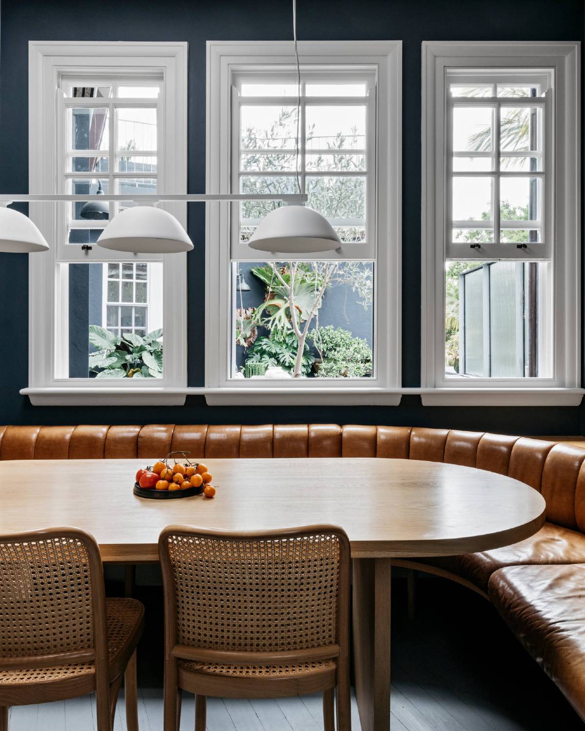 tan leather curved banquette seating in dark dining room rattan chairs