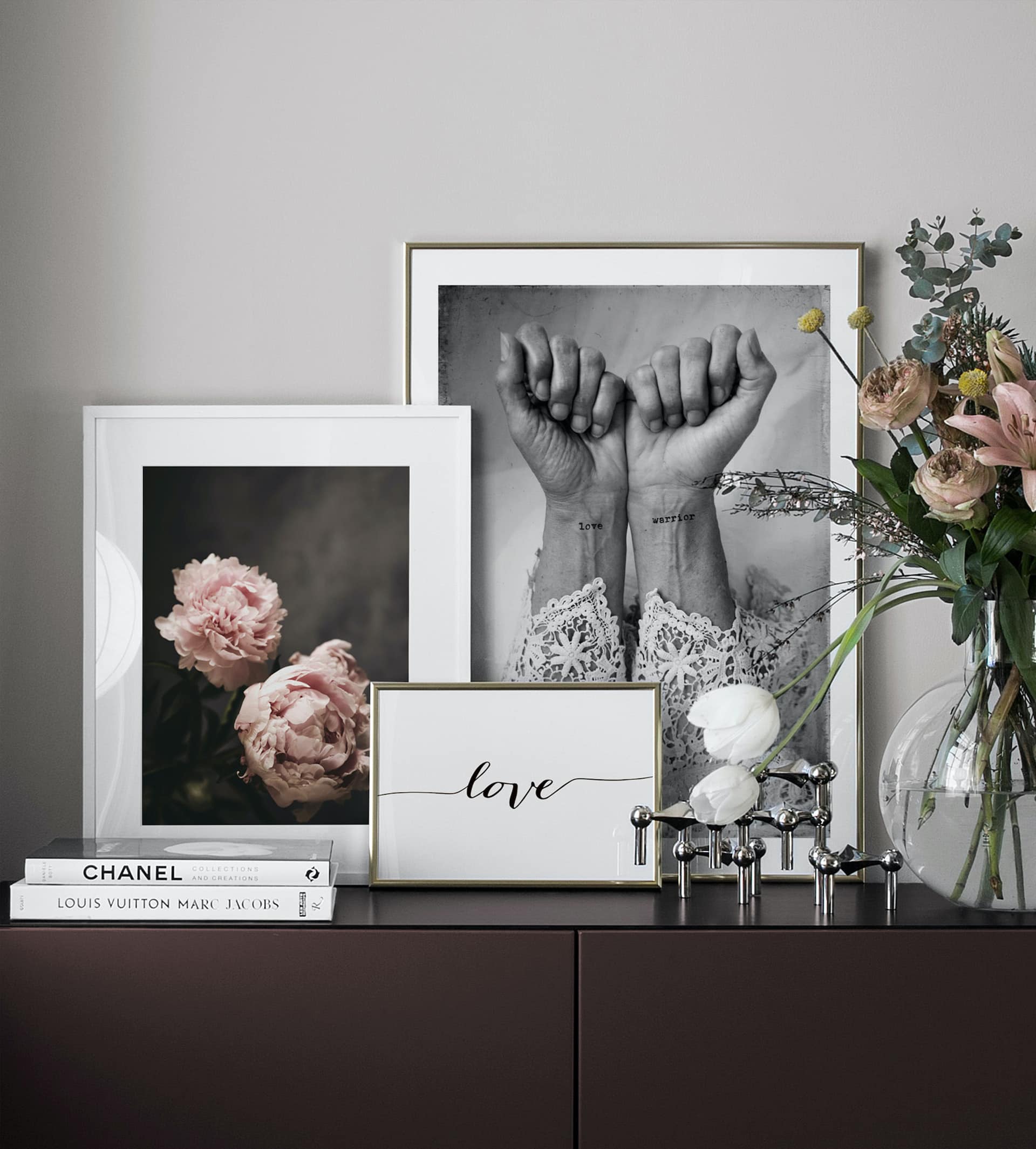 desenio art in thin gold frames leaning on dark brown sideboard
