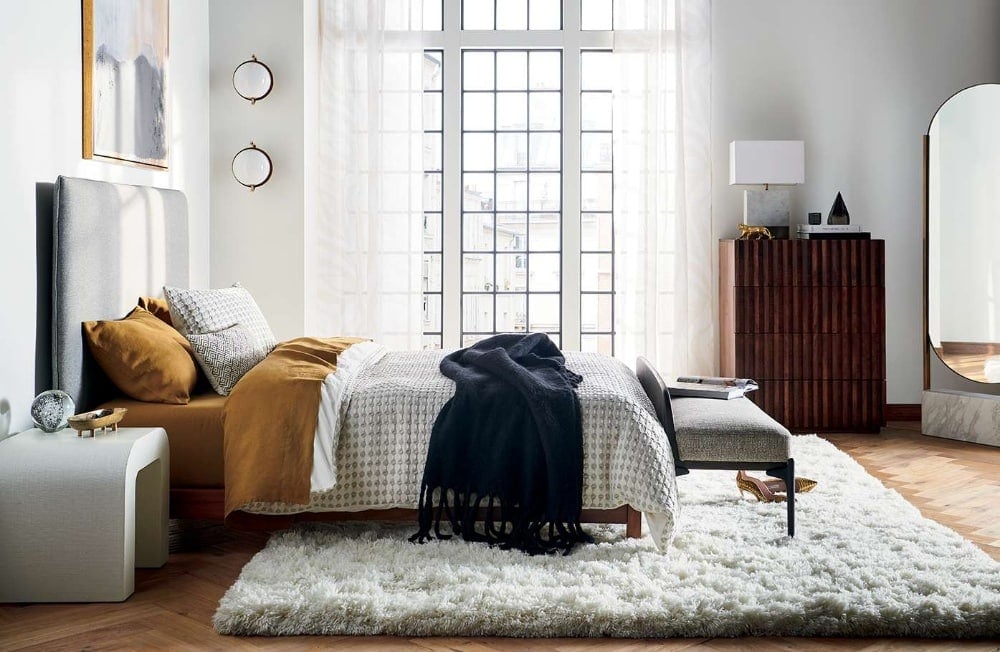 bedroom with mustard sheet set and tall windows with white sheer curtains