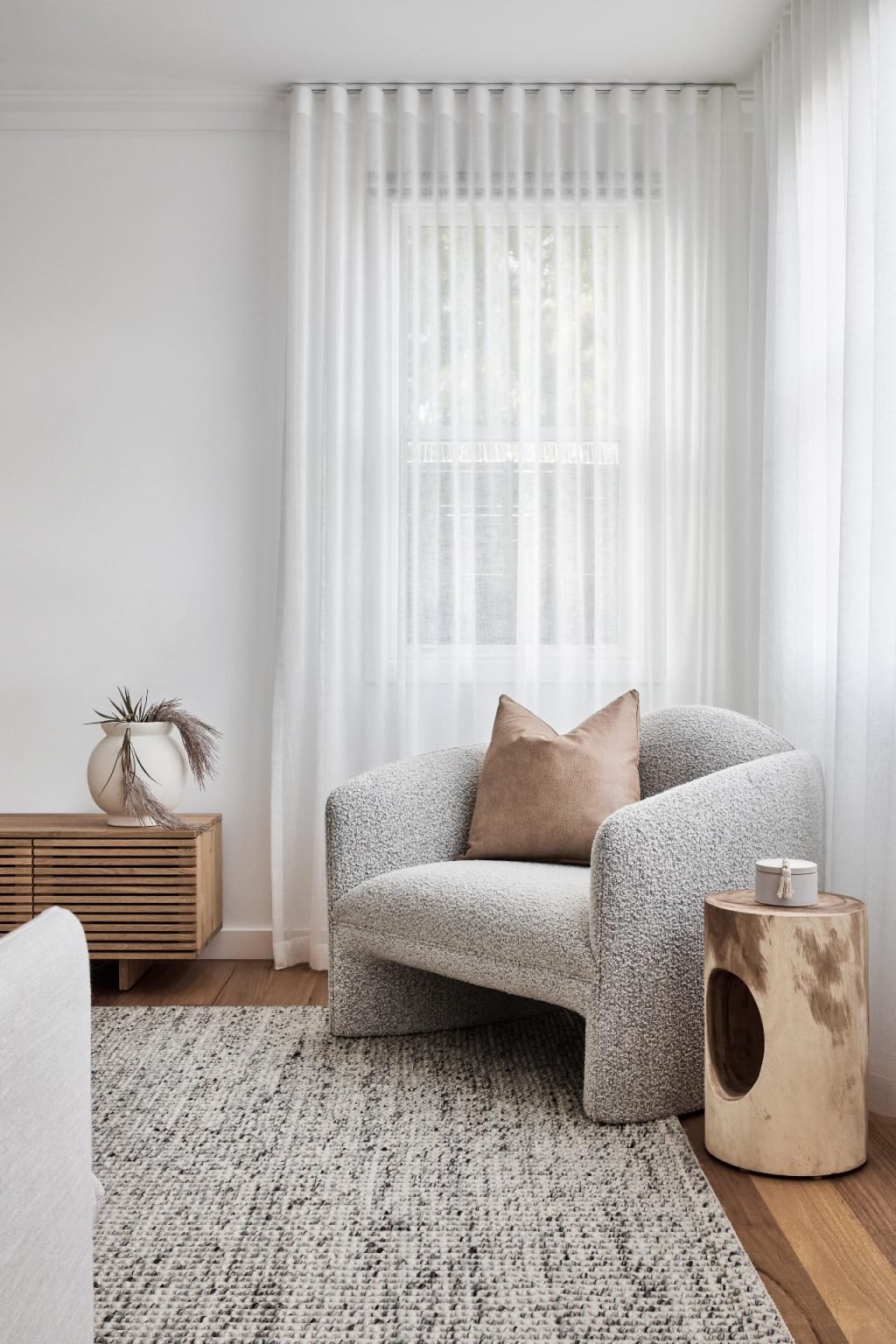 white boucle armchair in corner of living room with white sheer curtains and textured grey rug